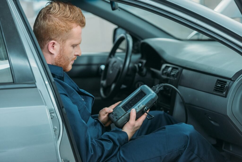 Automechanic sitting in a car, using a car diagnostic tool